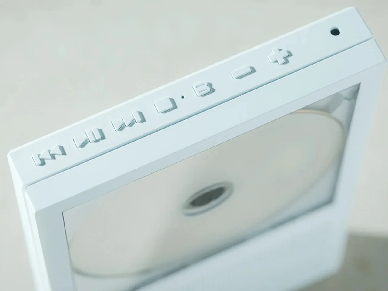 Close-up of a white media drive with a circular disc in the tray and embossed buttons along the top edge.
