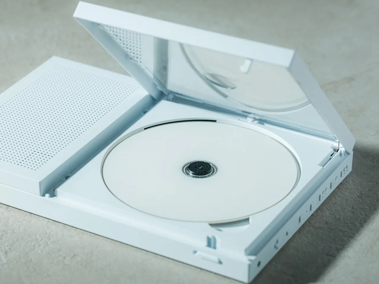 Open white CD/DVD drive with a blank disc in the tray on a light surface